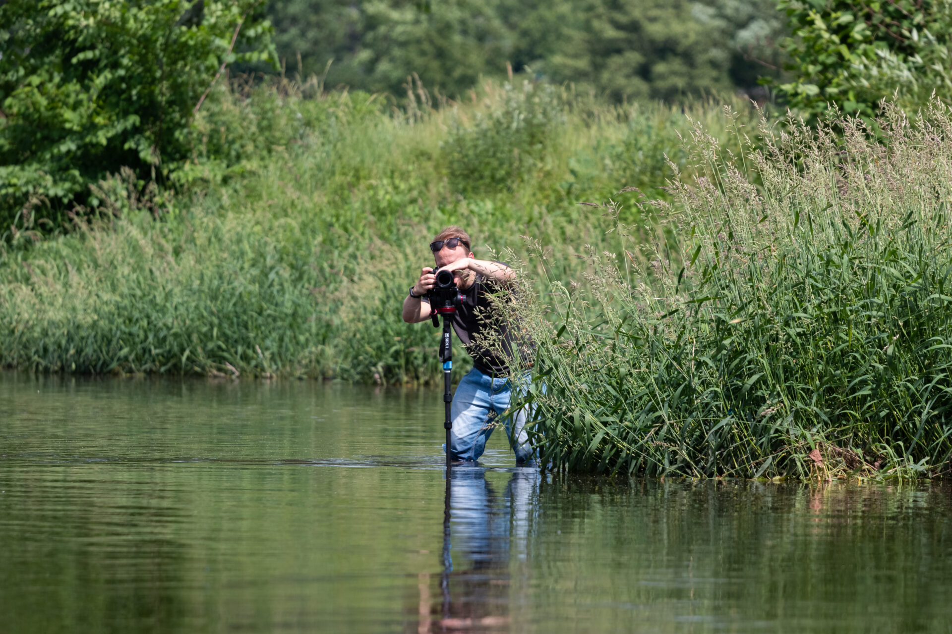 Kameramann Leon Petzoldt steht bis zu den Knien im Wasser und macht Filmaufnahmen