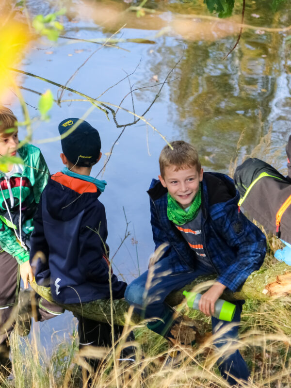 Junge Naturwächter sitzen auf einem Baum am Wasser