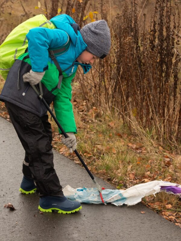 Junger Naturwächter sammelt Müll vom Wegrand auf