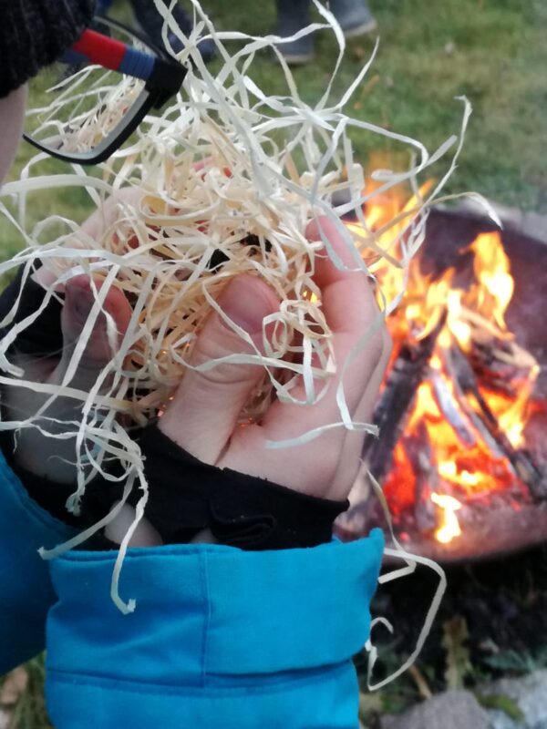 Ein Junger Naturwächter mit einem Zundernest in der Hand vor einem Lagerfeuer