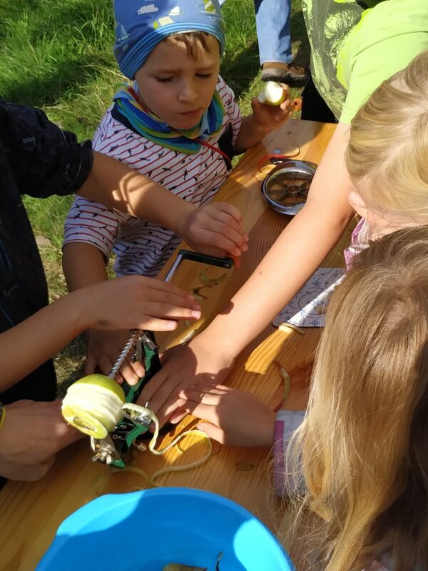 Kinder stehen gemeinsam um ein Gerät, dass eine Apfel schält